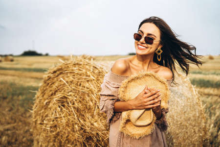 Smiling woman in sunglasses with bare shoulders on a background of wheat field and bales of hay.の写真素材