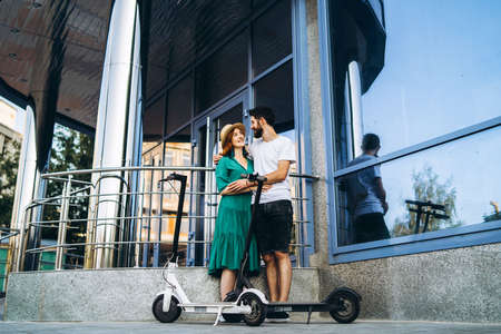 A young woman in dress and man talking to each other and enjoy a convenient way to travel around the city on electric scooters.の写真素材