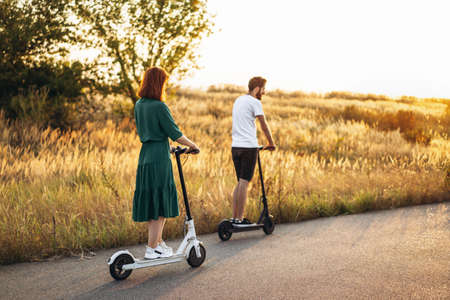 Young couple on vacation having fun driving electric scooter on the road in the countryside. Content technologies. Back view.の写真素材