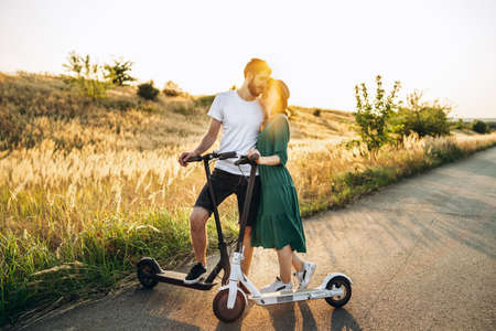 Portrait of young couple at sunset with beautiful natural landscape. Walking on electric scooters in the countryside.の写真素材