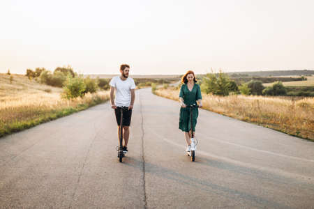 Young happy smiling couple having fun driving electric scooter on the road in the countryside. Content technologies.の写真素材