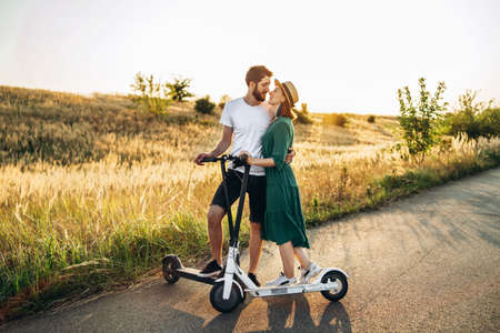 Portrait of young couple at sunset with beautiful natural landscape. Walking on electric scooters in the countryside.の写真素材