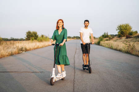 Young happy smiling couple having fun driving electric scooter on the road in the countryside. Content technologies.の写真素材