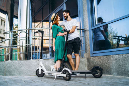 A young woman in dress and man talking to each other and enjoy a convenient way to travel around the city on electric scooters.の写真素材