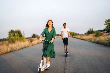 Young happy smiling couple having fun driving electric scooter on the road in the countryside. Content technologies.の写真素材
