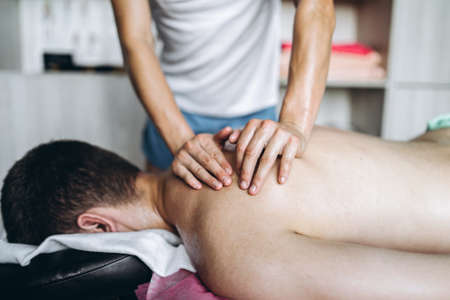 A woman physiotherapist doing back massage for a man in the medical office. Closeup of hands doing massage.の写真素材