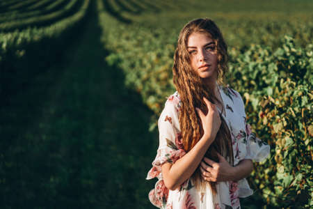 beautiful woman with long curly hair and freckles face on currant field background. Girl in a light dress walks in the summer sunny day.の写真素材
