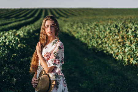 beautiful woman with long curly hair and freckles face on currant field background. Girl in a light dress walks in the summer sunny day.の写真素材