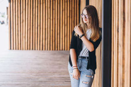Portrait of a young woman on the wooden background with vertical boards. Beautiful girl with long hair and glasses smiling.の写真素材