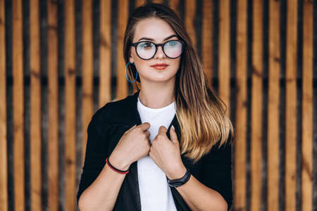 Portrait of a young woman on the wooden background with vertical boards. Beautiful girl with long hair and glasses smiling.の写真素材