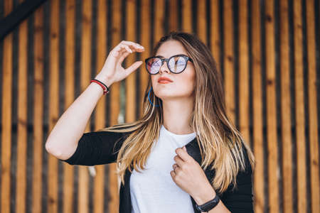Portrait of a young woman on the wooden background with vertical boards. Beautiful girl with long hair and glasses smiling.の写真素材