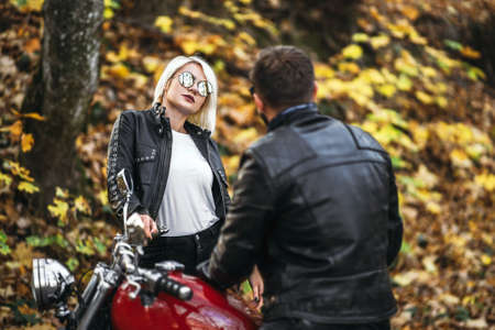 Pretty couple near red motorcycle on the road in the forest with colorful blured background. Relationship concept.の写真素材