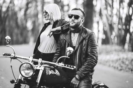 Black and white photo of pretty couple near motorcycle on the road in the forest with blured background. Relationship concept.の写真素材