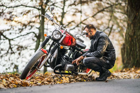 Bearded brutal man in sunglasses and leather jacket sitting on a motorcycle on the road in the forest with blured colorful background.の写真素材