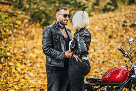 Pretty couple near red motorcycle on the road in the forest with colorful blured background. Relationship concept.の写真素材