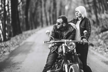 Black and white photo of pretty couple near motorcycle on the road in the forest with blured background. Relationship concept.の写真素材
