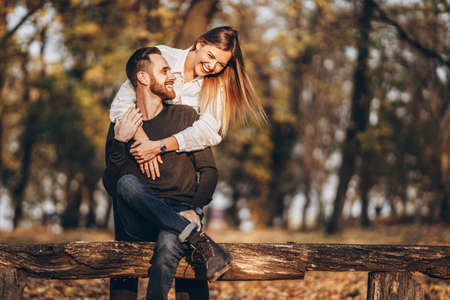 A young loving couple sitting on a wooden bench in the forest. Man and woman hugging and smiling on the background of autumn trees.の写真素材
