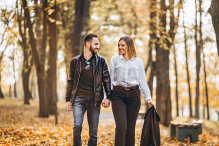 Portrait of a happy loving couple walking outdoor in the autumn park. Man and woman holding hands and smilling.の写真素材