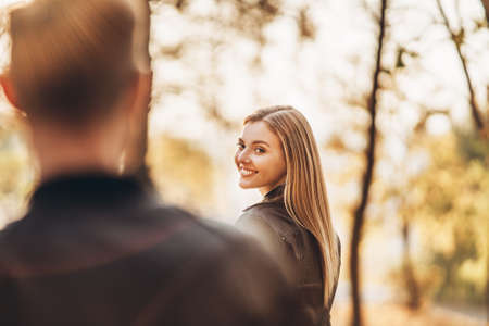 Portrait of a young smilling woman on the background of autumn park. In the foreground a blurred silhouette of a man.の写真素材