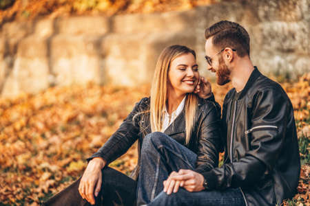 Portrait of a young loving couple, sitting in autumn leaf and enjoying nature. Love story.の写真素材