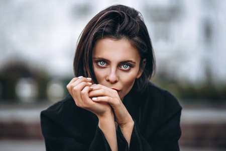 Close up portrait of young woman with short haircut and red lips, dressed in black. Woman posing on a blurred urban background.の写真素材