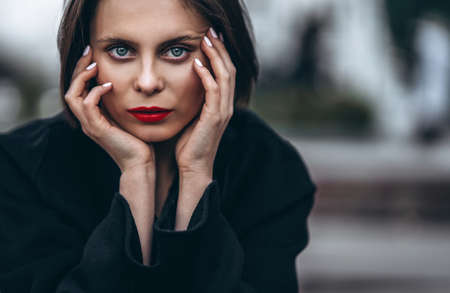 Close up portrait of young woman with short haircut and red lips, dressed in black. Woman posing on a blurred urban background.の写真素材