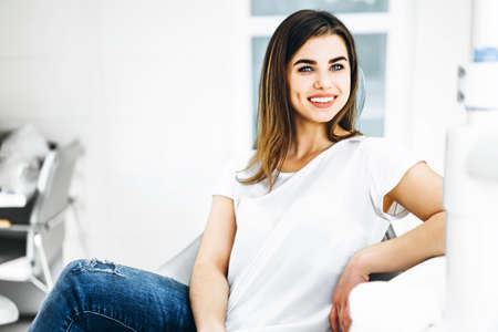 Pretty happy and smiling dental patient sitting in the dental chair at the dental officeの写真素材