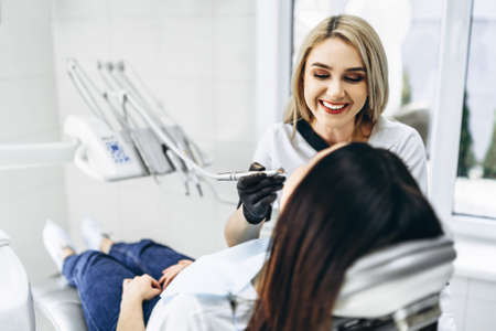 Pretty young female dentist making examination and treatment for young female patient in dental clinicの写真素材