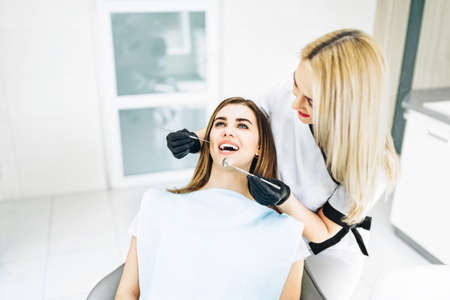 Pretty young female dentist making examination and treatment for young female patient in dental clinicの写真素材
