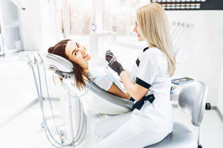 Pretty young female dentist making examination and treatment for young female patient in dental clinicの写真素材