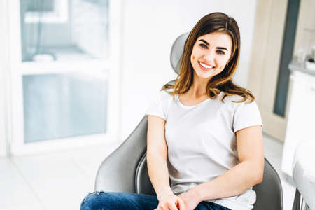 Pretty happy and smiling dental patient sitting in the dental chair at the dental officeの写真素材