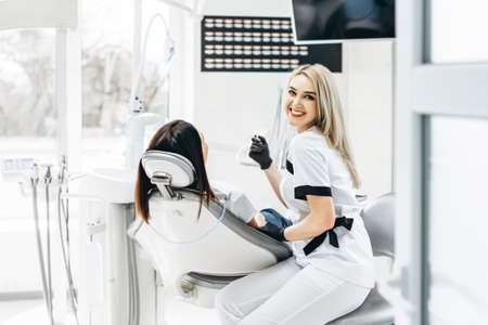 Pretty young female dentist making examination and treatment for young female patient in dental clinicの写真素材
