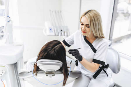 Pretty young female dentist making examination and treatment for young female patient in dental clinicの写真素材
