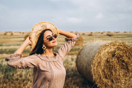 Smiling woman in sunglasses with bare shoulders on a background of wheat field and bales of hay.の写真素材