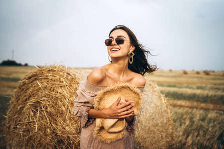 Smiling woman in sunglasses with bare shoulders on a background of wheat field and bales of hay.の写真素材