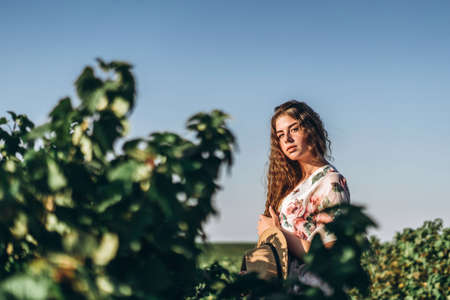 beautiful woman with long curly hair and freckles face on currant field background. Girl in a light dress walks in the summer sunny day.の写真素材