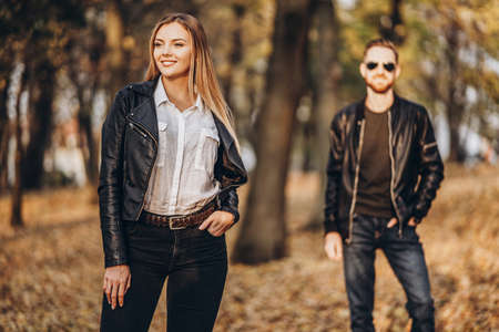 Beautiful young woman posing in autumn park. I the background is a blurred silhouette of her boyfriend. Love story.の写真素材