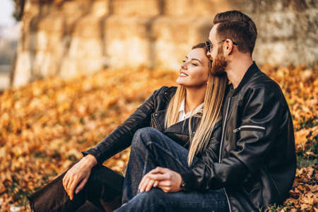 Portrait of a young loving couple, sitting in autumn leaf and enjoying nature. Love story.の写真素材