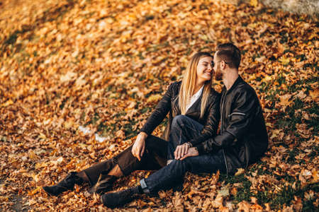 Portrait of a young loving couple, sitting in autumn leaf and enjoying nature. Love story.の写真素材