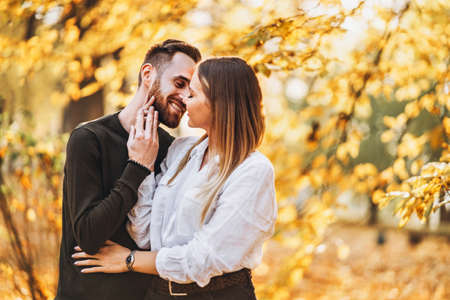 Sunny portrait of a young loving couple walking in the autumn park. They hug and smile, enjoy a walk.の写真素材
