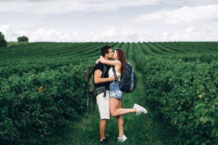 Portrait of happy young couple with backpacks on the field in spring. Man and woman walking in currant plantations.の写真素材