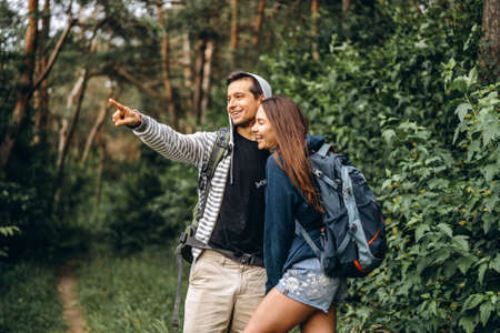 Young couple with backpacks on their backs smiling and walking in the forest, enjoy the walk.の写真素材