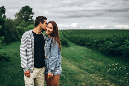 Young loving couple, woman and man, gently hugging with eyes closed on the background of green field. Love Story.の写真素材