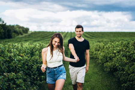 A tender loving couple walking in a field of currant. A smiling woman with long hair leads a man, holding his hand.の写真素材