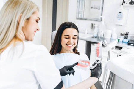 Pretty female dentist explaining way of treatment on the denture for the patient in the clinic