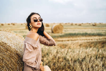 Smiling woman in sunglasses with bare shoulders on a background of wheat field and bales of hay.の写真素材