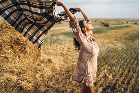 Portrait of a beautiful brunette in a dress and with a warm plaid. Woman enjoying a walk in a wheat...