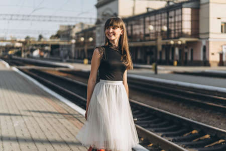 Female brunette traveler with red suitcase in white skirt waiting for a train and walking on raiway stationの写真素材