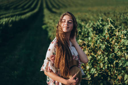 beautiful woman with long curly hair and freckles face on currant field background. Girl in a light dress walks in the summer sunny day.の写真素材