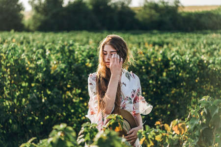beautiful woman with long curly hair and freckles face on currant field background. Girl in a light dress walks in the summer sunny day.の写真素材